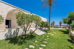 A building with a stone facade, a staircase leading to the entrance, and a well-maintained lawn with palm trees.
