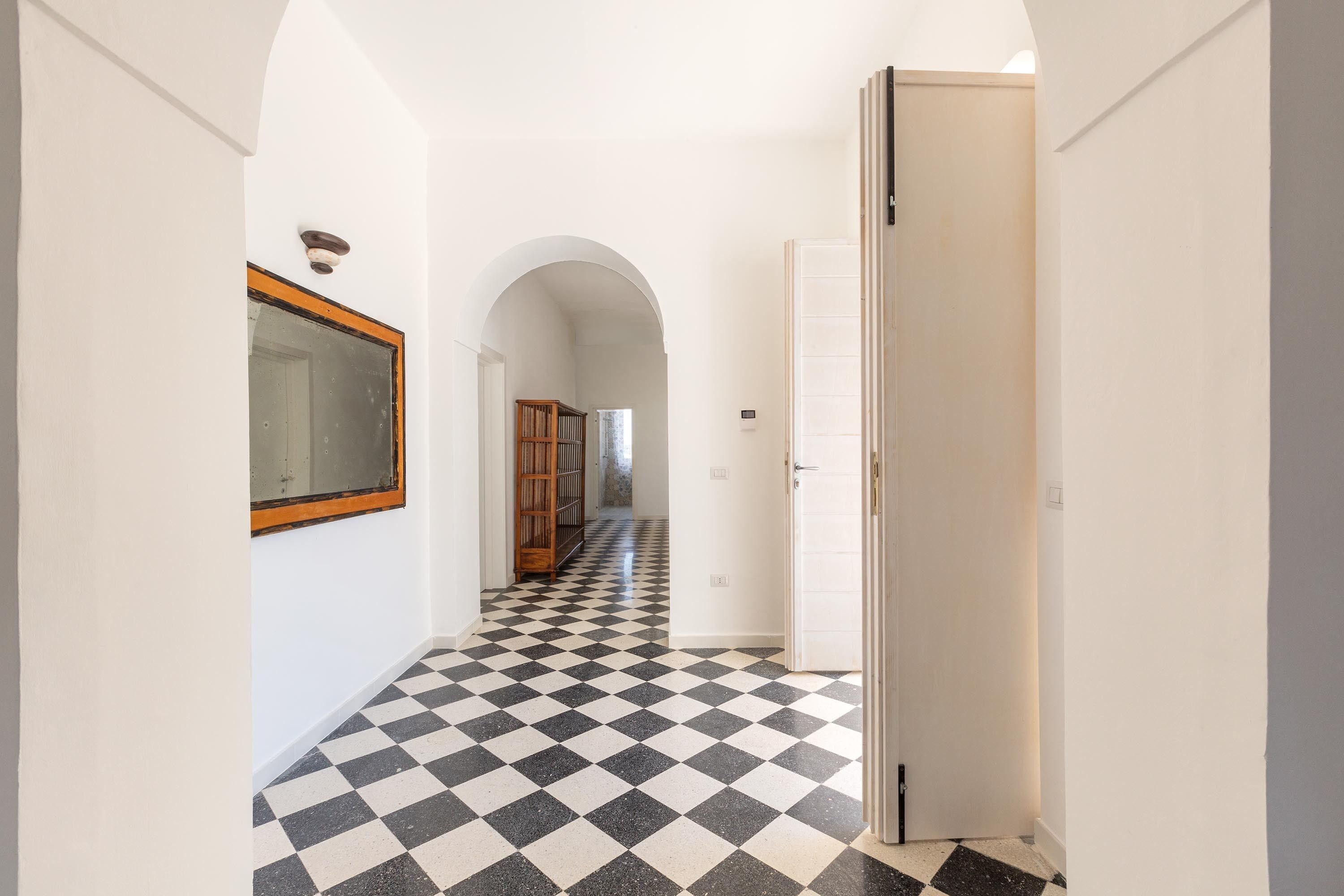A hallway with a checkered floor, a door on the right, and a wooden bookshelf in the background.