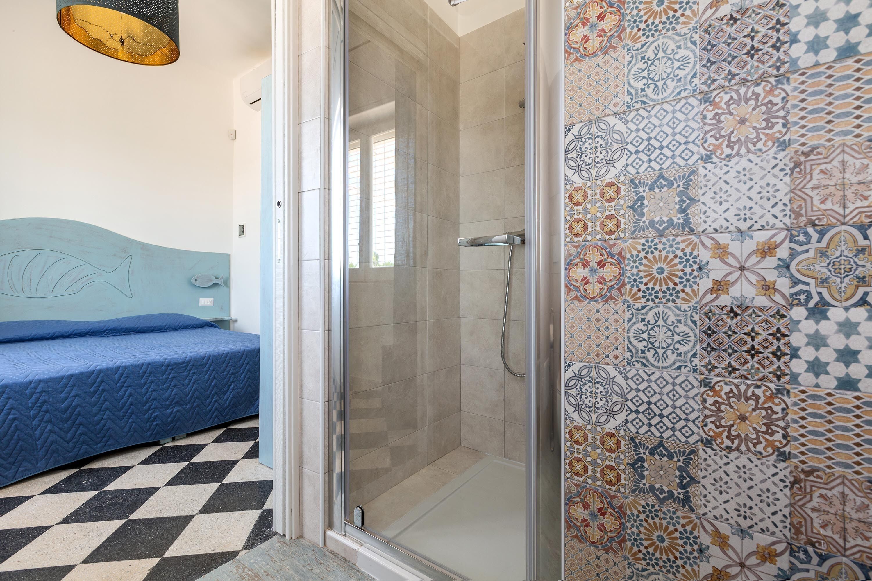 Una habitación con cama, zona de ducha y pared de azulejos con un diseño decorativo.