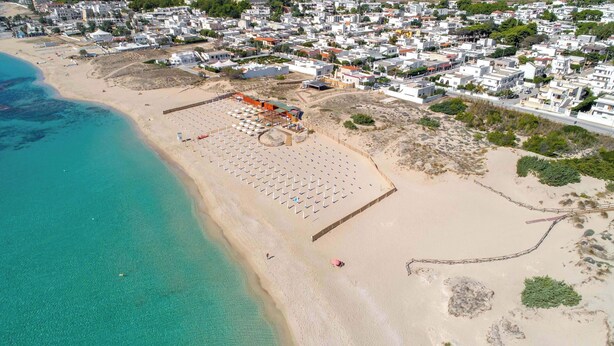 An aerial view of a coastal area with a beach, a row of white buildings, and a clear blue sea. - 2494 Villa Tina Maria by Perle di Puglia (Manduria)