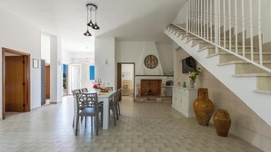 A spacious living area with a fireplace, a staircase, and a dining area with chairs and a table. - 2494 Villa Tina Maria by Perle di Puglia (Manduria)