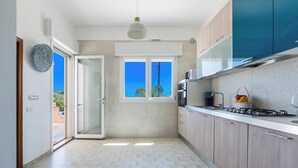 A modern kitchen with a sliding glass door leading to a balcony, a built-in stove, and a view of the sky. - 2494 Villa Tina Maria by Perle di Puglia (Manduria)