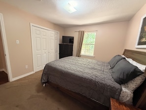 A bedroom with a bed, a wardrobe, a television, a window with curtains, and a ceiling light.