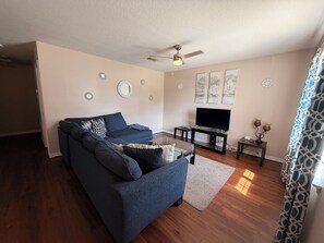A living room with a dark blue sofa, a glass coffee table, a flat-screen TV, and decorative wall mirrors.