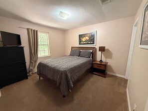 A bedroom with a bed, dresser, window, and artwork on the wall.