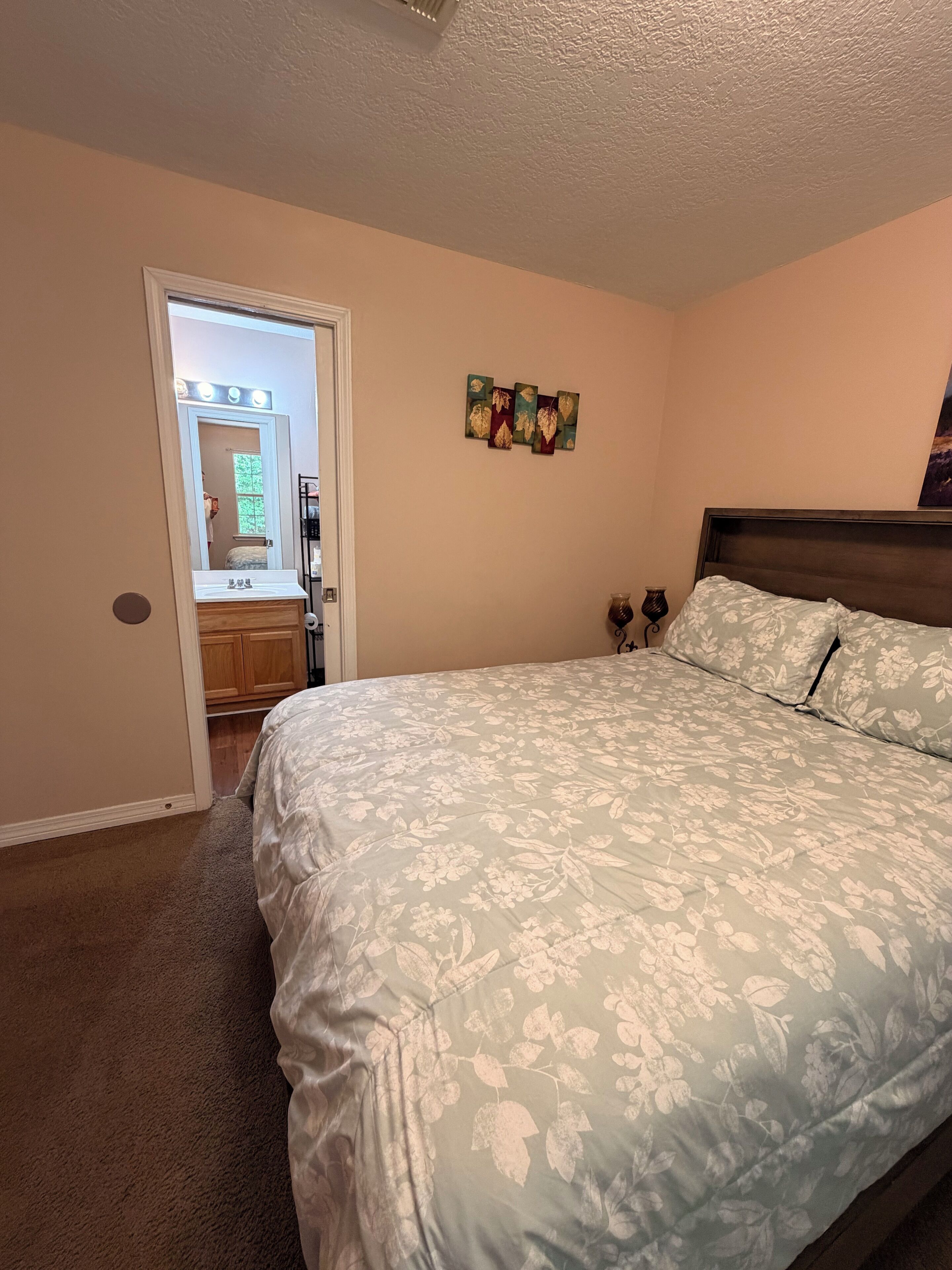 Une chambre à coucher comprenant un lit, une commode, une coiffeuse avec un miroir et une porte donnant sur une autre pièce.