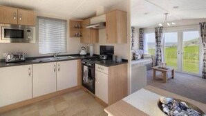 Una cocina moderna con armarios de madera, microondas y estufa. Hay un comedor con una mesa y sillas, y vistas a un paisaje verde a través de amplias ventanas.
