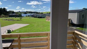 Vista de un camping con vehículos recreativos y casas móviles, una zona con césped y una masa de agua al fondo.