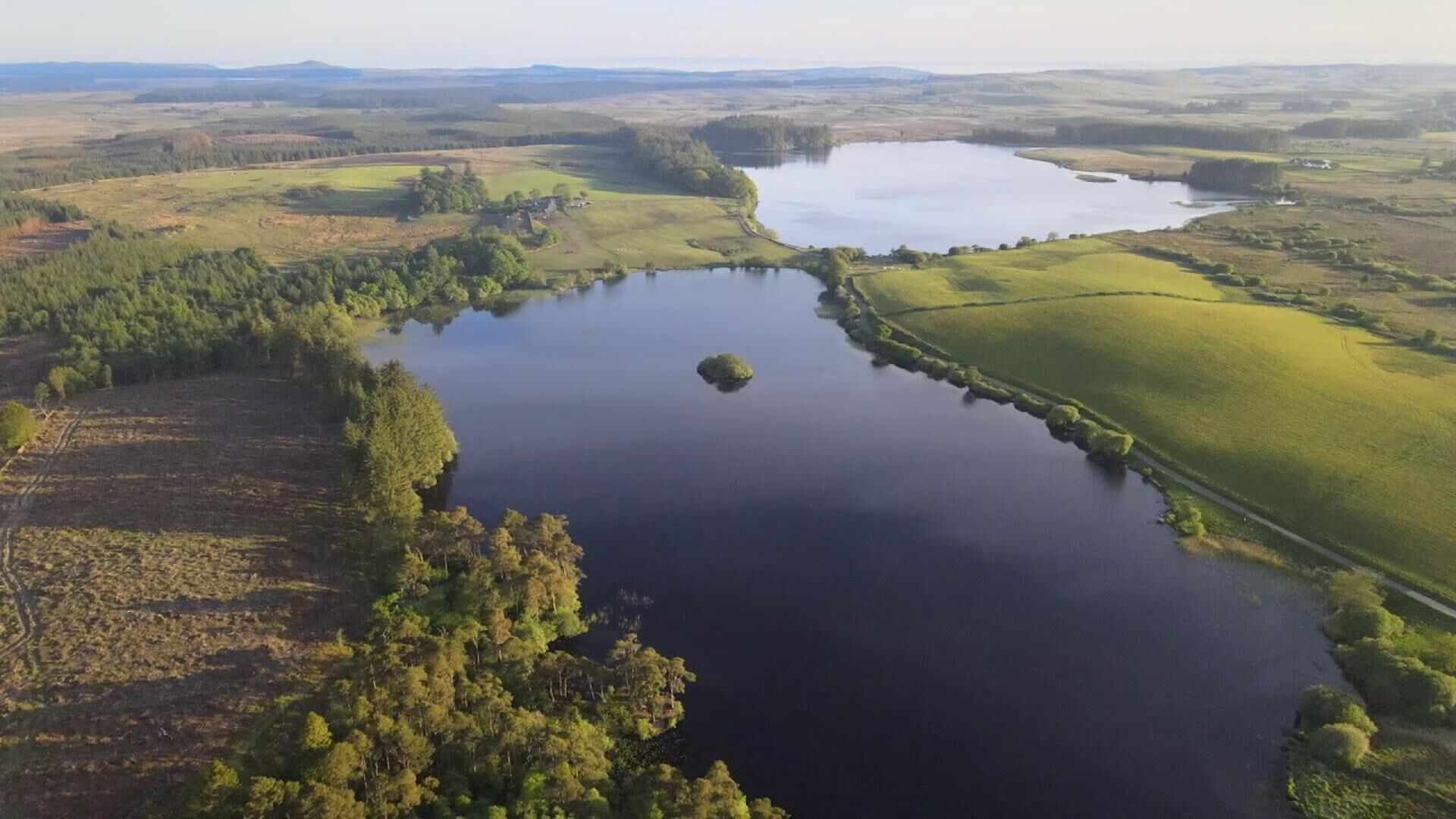 An aerial view of a lake surrounded by forested areas and open fields.