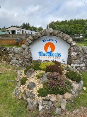 A welcome sign for Three Lochs Holiday Park surrounded by a stone wall and greenery. - 3 Bedrooms Loch Views Heated Pool Close To Beaches (Newton Stewart)