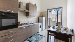 A modern kitchen with a built-in oven, microwave, and washing machine. There is a dining table with bowls and a spoon. - 2934 Villetta Patrizia - Bilocale by Barbarhouse (Manduria)