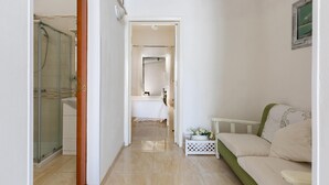 A narrow hallway leading to a bedroom with a bed, a small table with flowers, and a shower area. - 2934 Villetta Patrizia - Bilocale by Barbarhouse (Manduria)