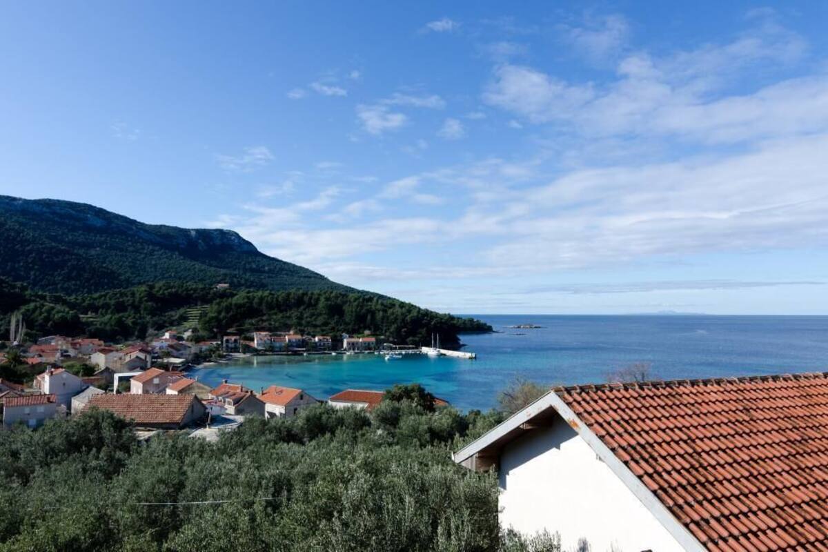 Un pueblo costero con casas, un mar azul cristalino y un paisaje montañoso al fondo.