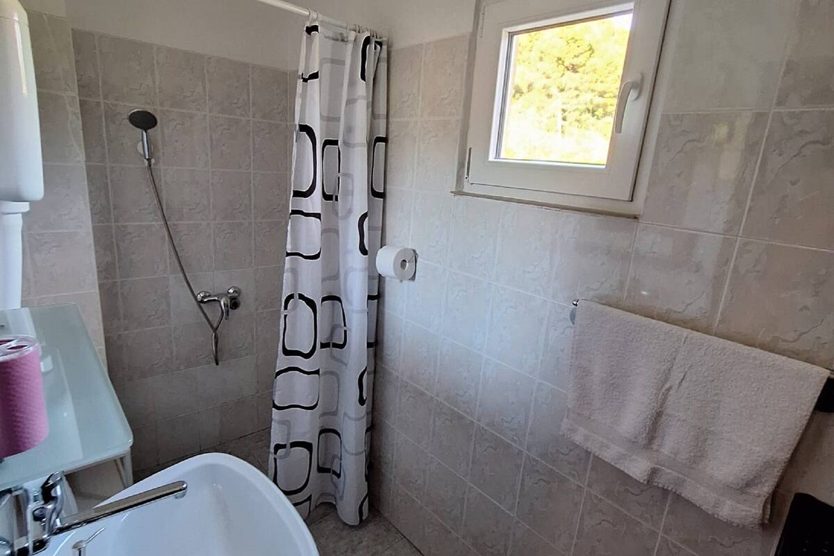 Un baño con ducha, lavabo, ventana y toallero.