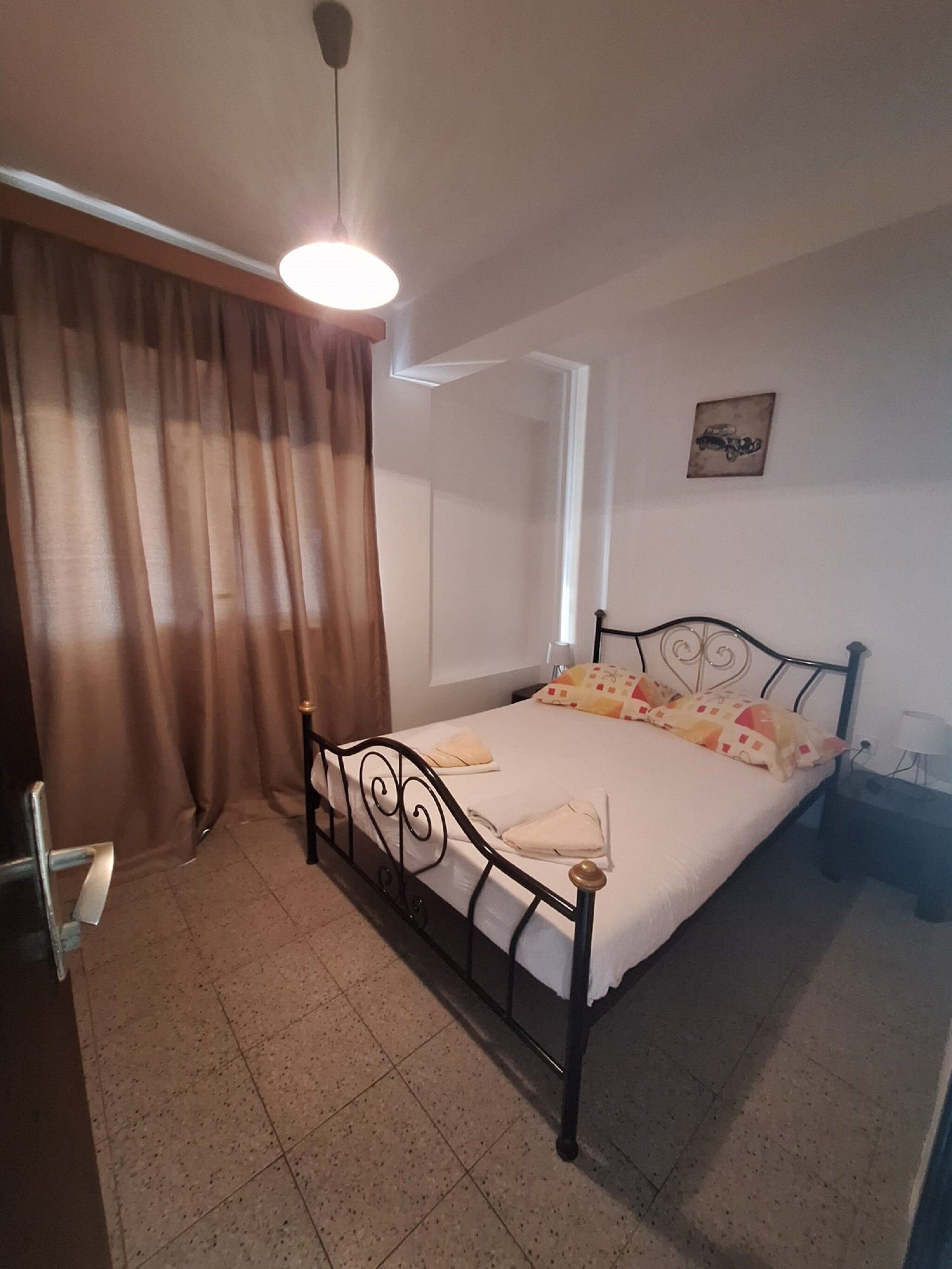 A single bed with a headboard, a bedside table, a lamp, a curtain, and a ceiling light fixture.