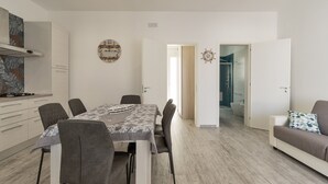 A modern kitchen with white cabinets, a dining table with chairs, and a view into the living area. - 2805 Villetta Anna by Barbarhouse (Porto Cesareo)