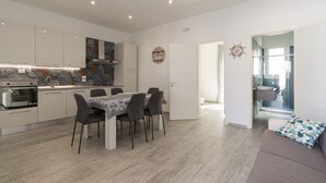 A modern kitchen with a dining area, wooden flooring, and a sofa with a patterned cushion. - 2805 Villetta Anna by Barbarhouse (Porto Cesareo)