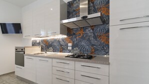 A modern kitchen with white cabinets, a stainless steel range hood, a gas stove, and a flat-screen TV mounted on the wall. - 2805 Villetta Anna by Barbarhouse (Porto Cesareo)