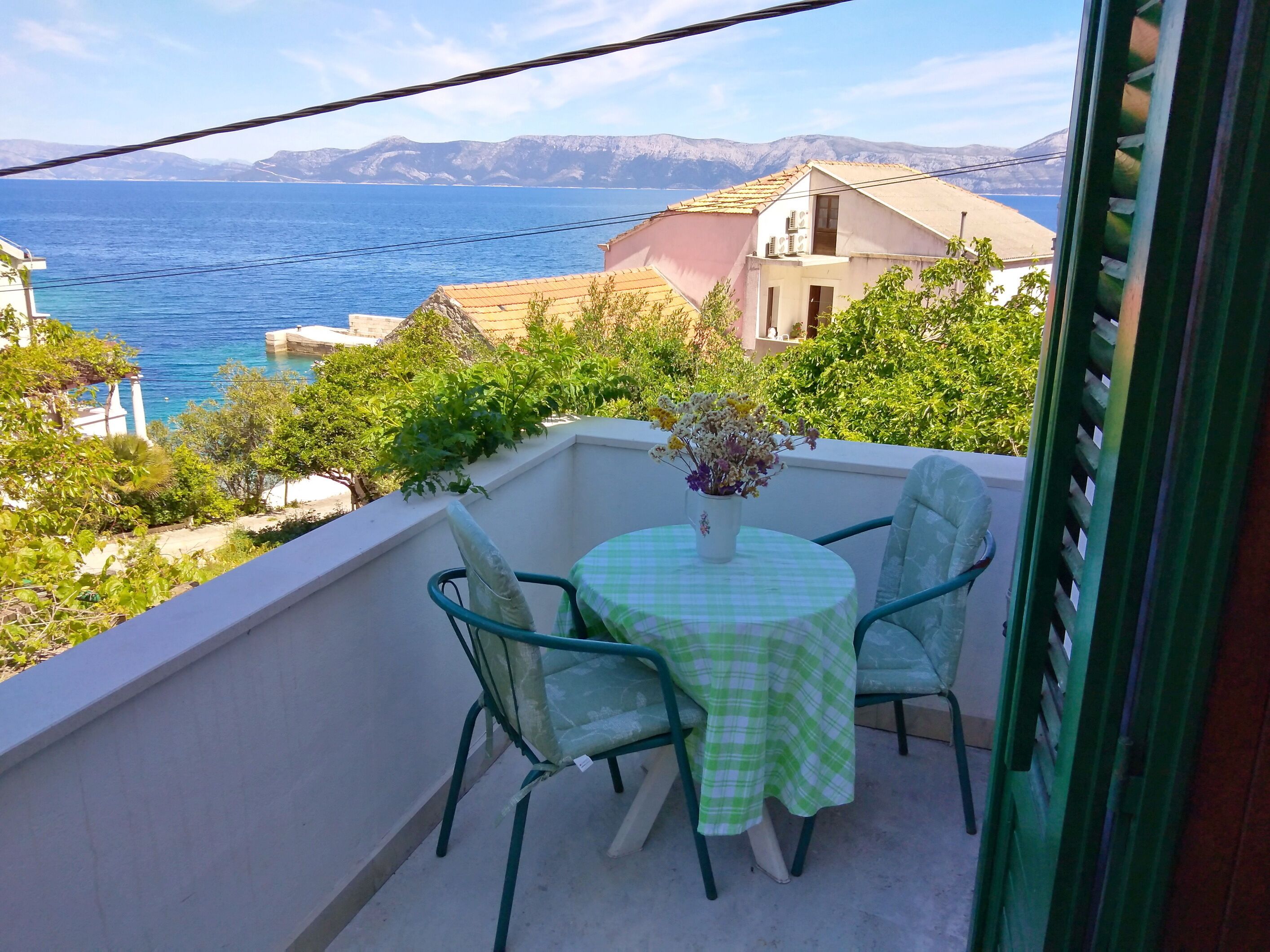 Balcón con mesa y sillas, con vista al mar y montañas a lo lejos.