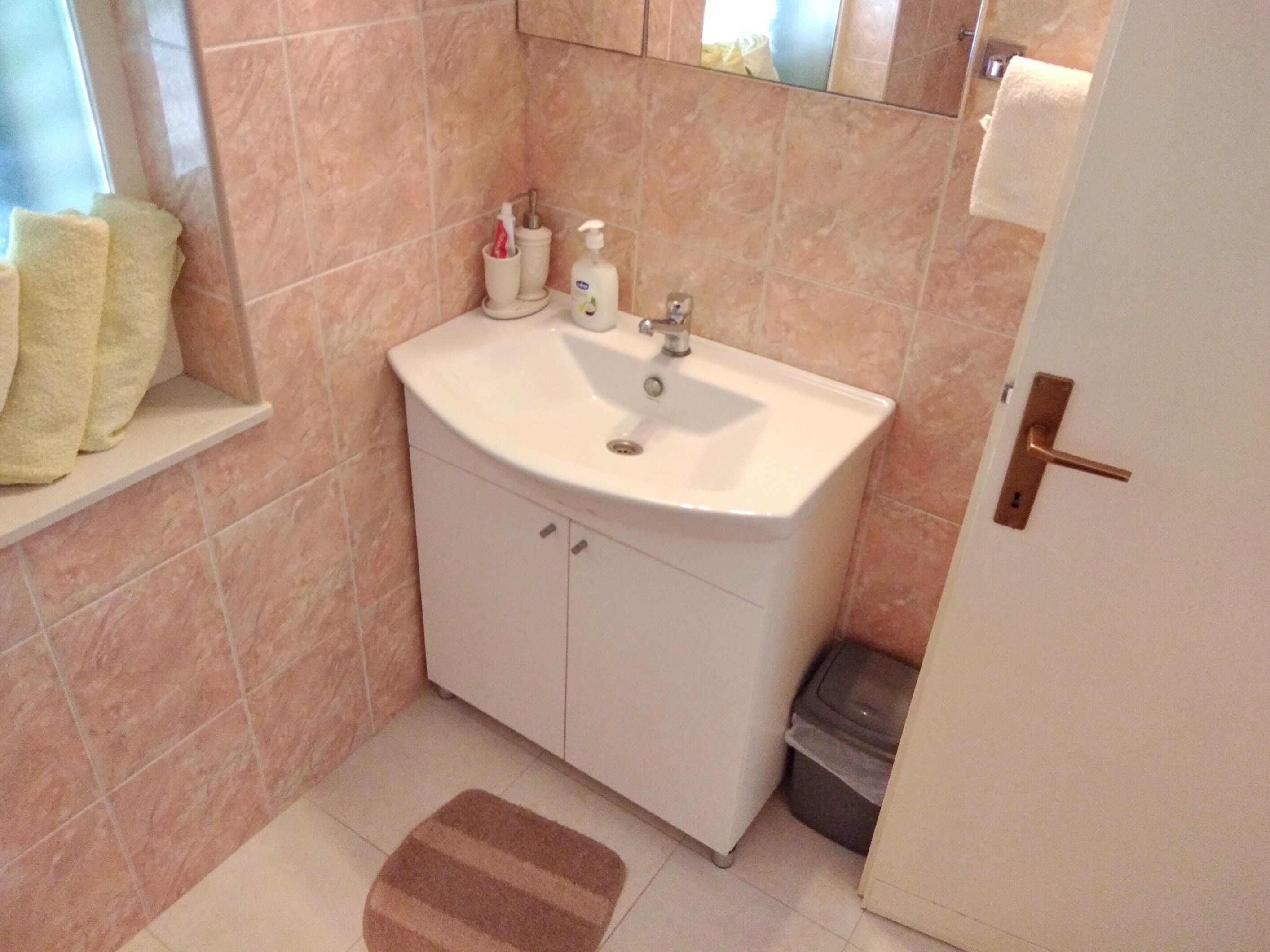 A bathroom with a sink, mirror, and a small trash bin.