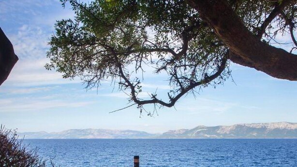 A table set for two with a bottle of wine, glasses, and plates, overlooking a body of water with mountains in the distance. - Guest House Hazdovac Rooms (Mljet)