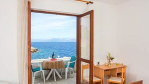 A room with a bed, a desk, and a table with chairs. There is a view of the sea through a glass door. - Guest House Hazdovac Rooms (Mljet)