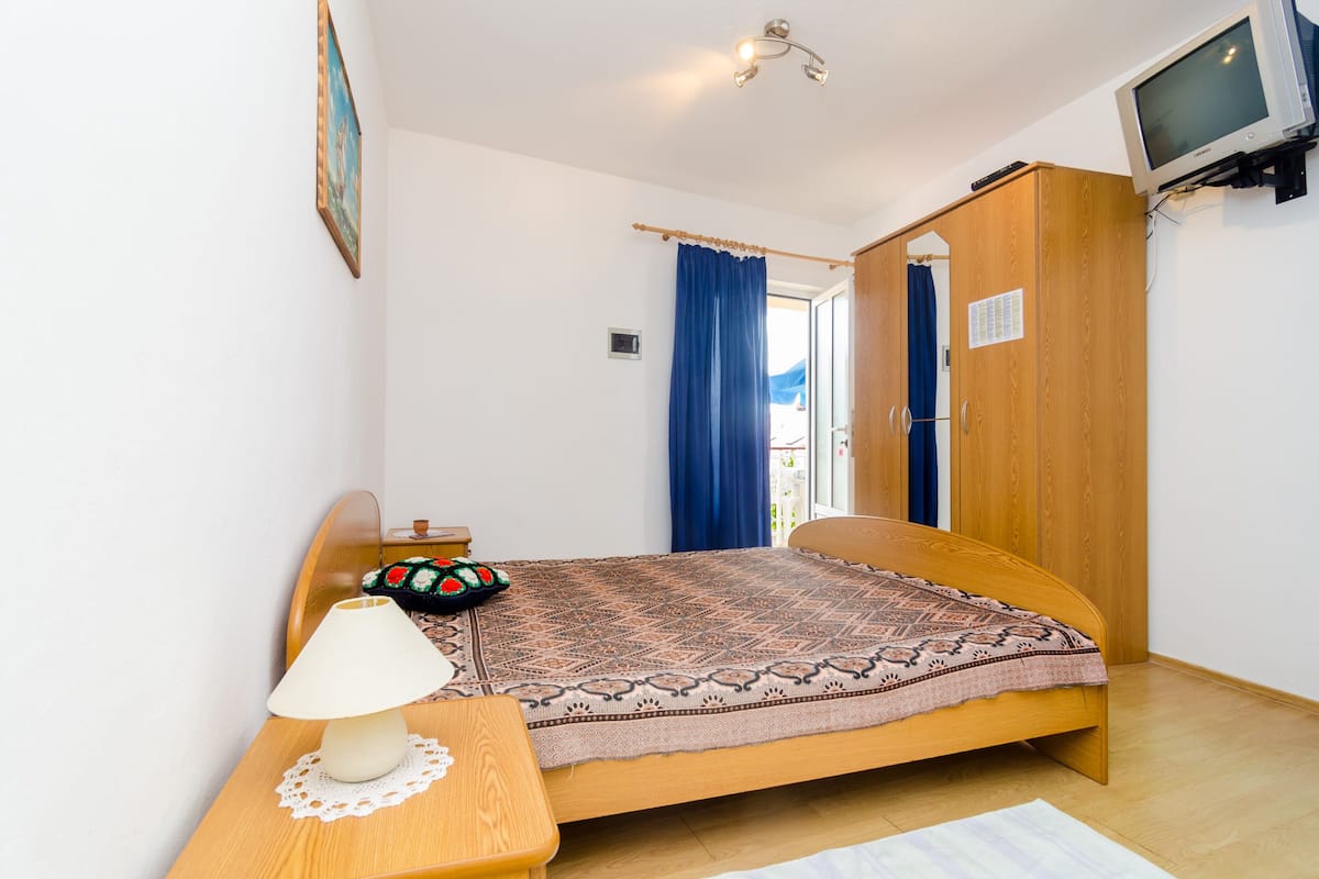 Un dormitorio con cama, mesita de noche con lámpara, armario y televisor.