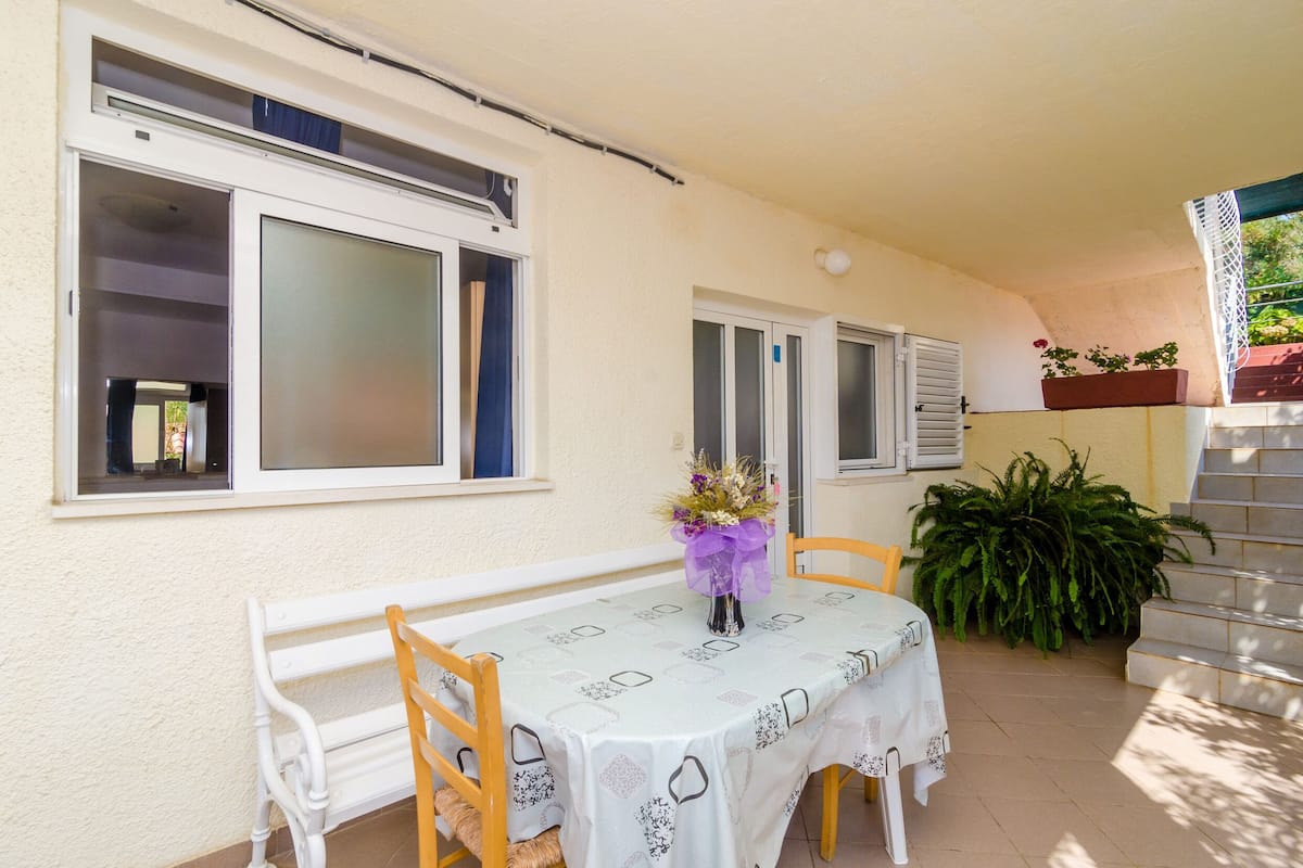 Un patio techado con una mesa y sillas, una ventana con persianas y una planta en maceta.