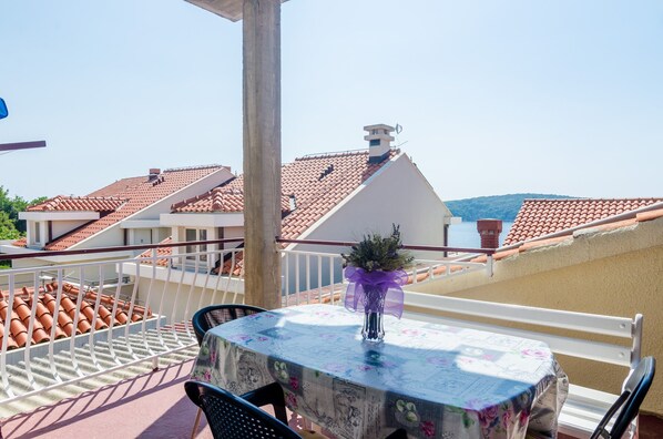 A terrace with a table and chairs, a vase with flowers, and a view of terracotta-roofed buildings.