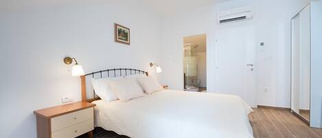 A bedroom with a bed, bedside tables, a nightstand, a wall-mounted picture, and an air conditioning unit.