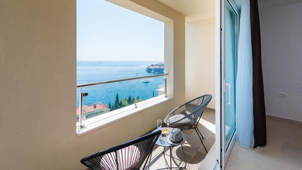 A balcony with a view of the sea, two chairs, and a small table.