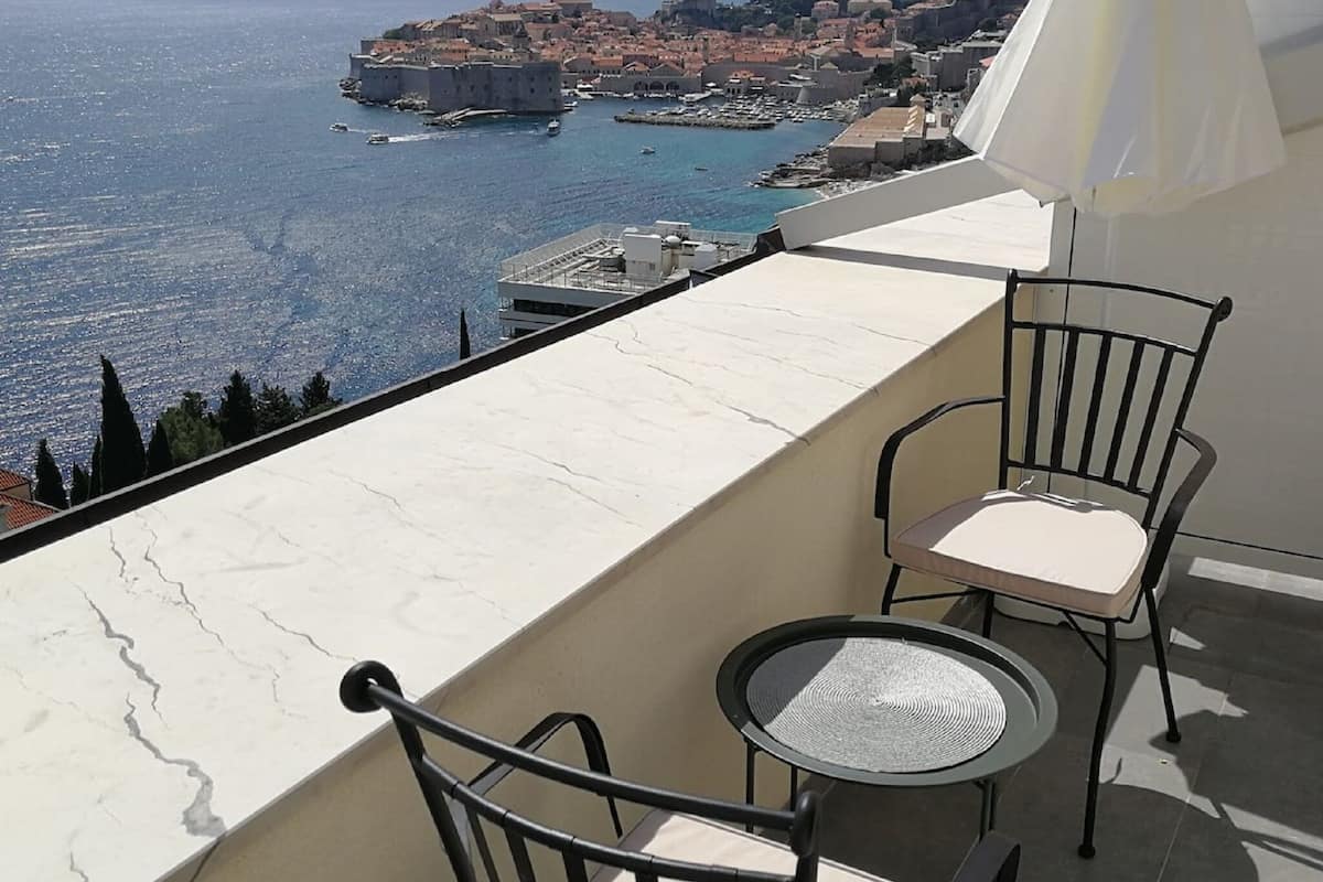 Varanda com vista para uma vila costeira, uma mesa e duas cadeiras.