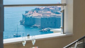 A room with a view of a coastal town, a table with a glass of wine, and a chair.