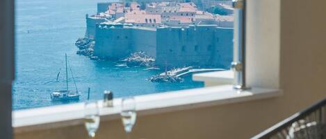 A room with a view of a coastal town, a table with a glass of wine, and a chair.