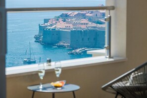 Enjoy a scenic view of the coastal town from this room's large window, with a dining area featuring a small table and a bowl of fresh fruit.