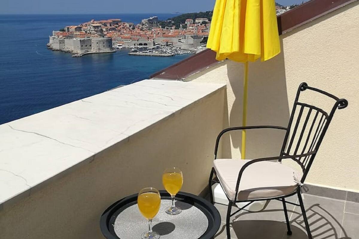 Varanda com mesa e duas cadeiras, com vista para uma cidade costeira.