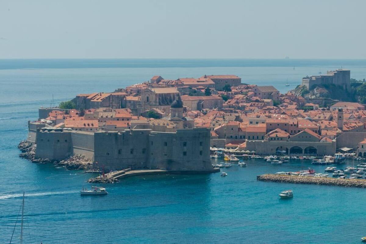 Uma cidade costeira com edifícios históricos, um castelo fortificado e um porto com barcos.