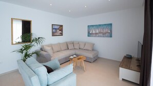 A modern living room with a light-colored sectional sofa, a small round table, and a wooden side table. There are two framed artworks on the walls and a potted plant.