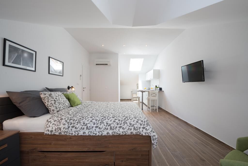 A modern bedroom with a wooden bed, a desk, and a TV mounted on the wall.