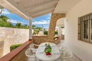 An outdoor patio with a stone wall, white chairs, and a table set for dining. - 2401 Villetta Rosa by Barbarhouse (Maruggio)