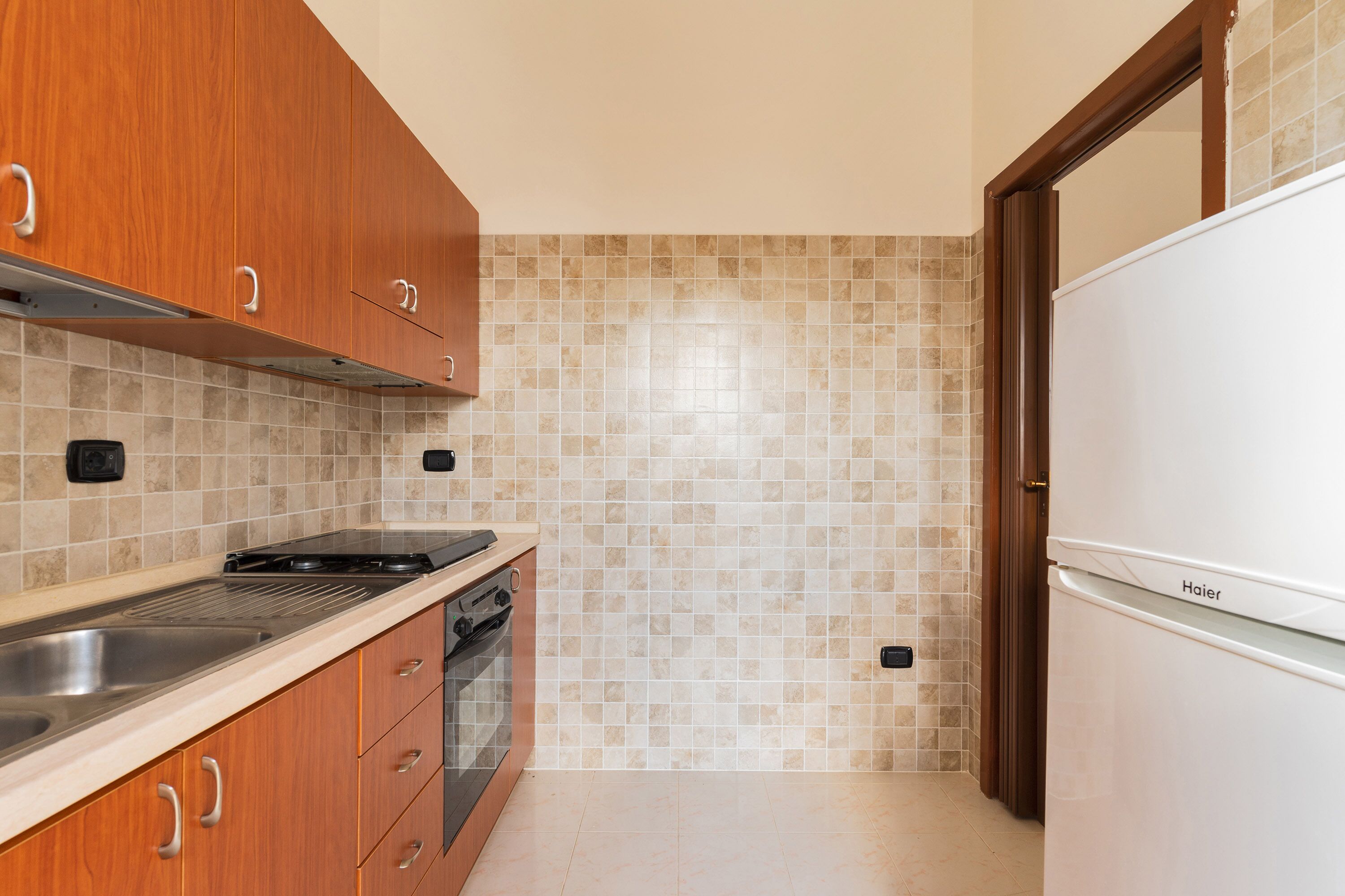 Una cocina con armarios de madera, un lavamanos de acero inoxidable, una estufa y un refrigerador blanco.