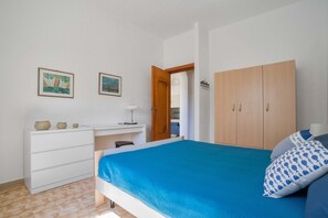 A bedroom with a bed, a desk, a wardrobe, and two framed pictures on the wall.