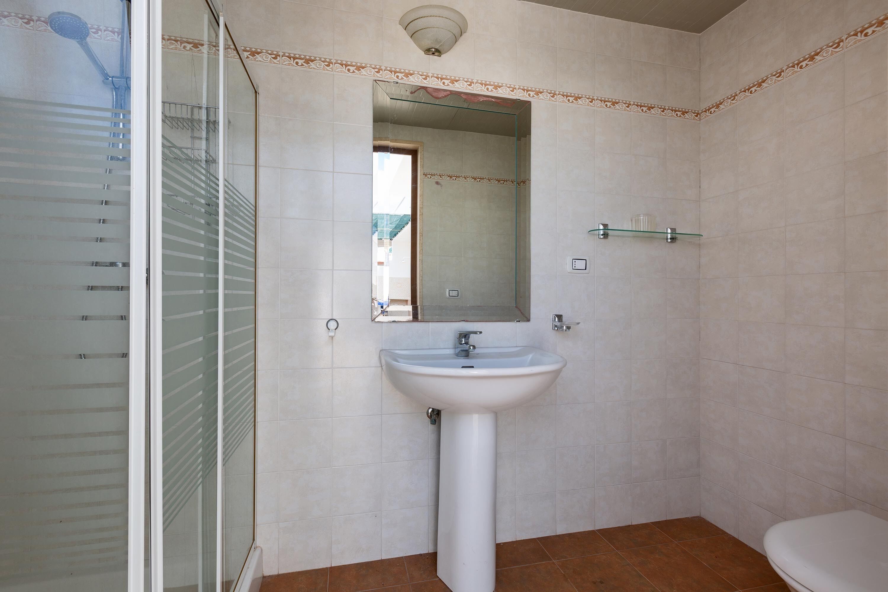 Un baño con cabina de ducha de vidrio, lavamanos pedestal y retrete.