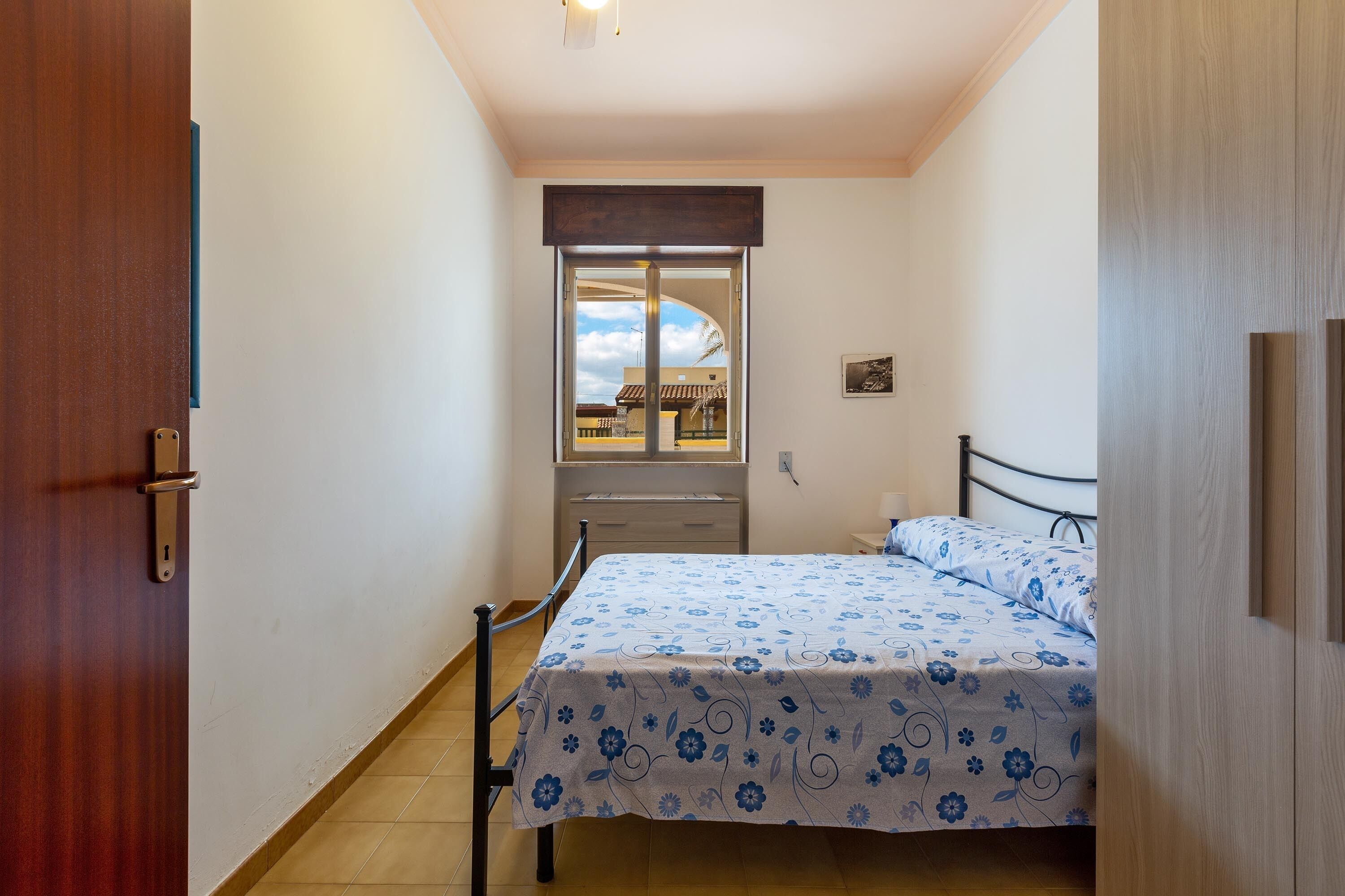 A bedroom with a bed, a window, a door, and a small bedside table.