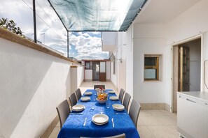 Un coin repas avec une table dressée pour quatre personnes, un espace cuisine et une vue sur un bâtiment en arrière-plan.