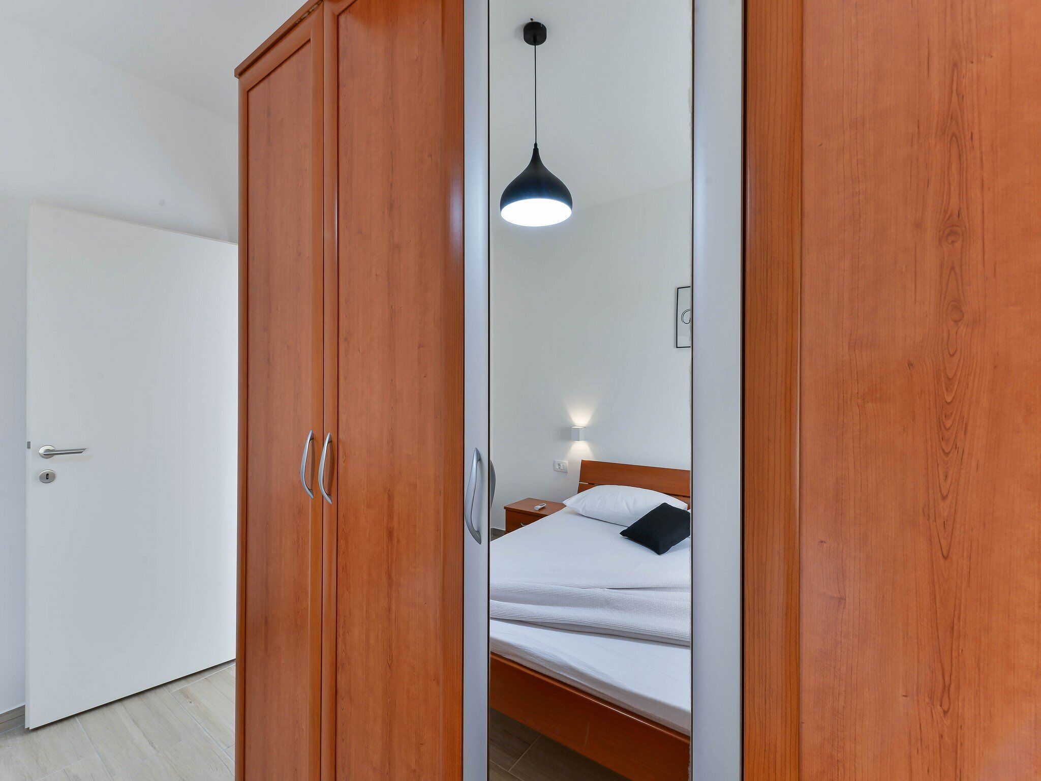 Un dormitorio con un armario de madera, una cama con ropa de cama blanca, una mesita de noche y una lámpara colgante.
