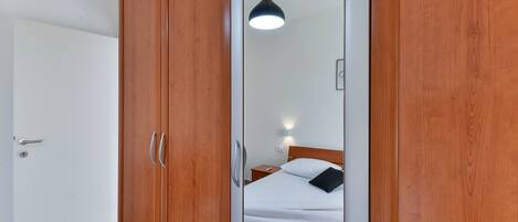 Un dormitorio con un armario de madera, una cama con ropa de cama blanca, una mesita de noche y una lámpara colgante.