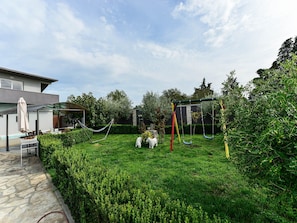 Un jardin avec une balançoire, un hamac et un patio couvert.