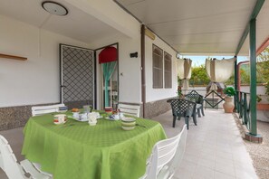 Uma área de varanda coberta com uma mesa posta para refeições, cadeiras e um vaso de planta.