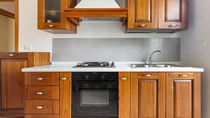 Una cocina con armarios de madera, horno empotrado, estufa a gas y pileta de acero inoxidable.